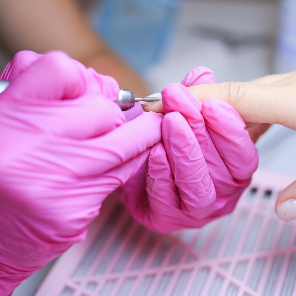 Close-up of a manicure procedure in a Polish salon with technician in pink gloves.
