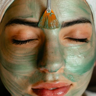 Close-up of a woman enjoying a green cosmetic facial mask application at a spa.