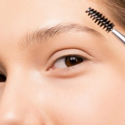 Close-up of a woman applying makeup with an eyebrow brush, highlighting natural beauty.