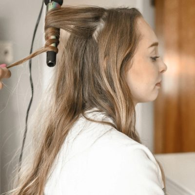 Profile of a woman having her hair curled with an iron in a salon setting.